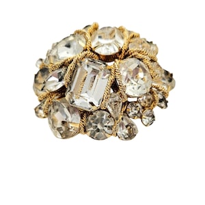 May include: A gold tone brooch with a cluster of clear rhinestones of various shapes and sizes.