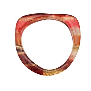 May include: A transparent, open-ended bangle bracelet with a rounded square shape. The bracelet features a blend of red, gold, and brown hues, with a marbled effect. The design incorporates gold leaf accents, creating a unique and artistic accessory.