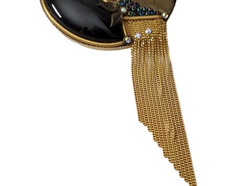 May include: A gold-toned brooch with a black stone and a long fringe of gold chains. The brooch is decorated with colorful rhinestones.