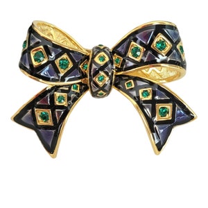 May include: A gold-tone bow brooch with black enamel and green rhinestones. The bow is decorated with a geometric pattern.