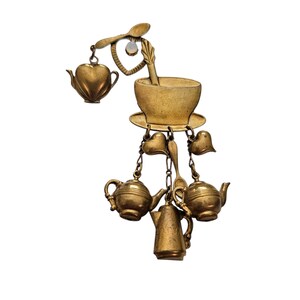 May include: A gold-toned brooch featuring a teacup, saucer, and spoon design. The brooch includes a heart-shaped teapot, dangling teapots, and hearts suspended by chains. The brooch is a vintage-style accessory.