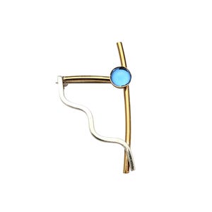 Puede incluir: Un broche único con un marco de metal dorado y un acento circular azul claro. El diseño incorpora un elemento ondulado plateado. Un accesorio elegante.