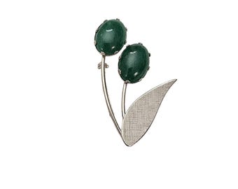 May include: A silver brooch with two green cabochon stones set in a flower design. The brooch has a leaf-shaped design.