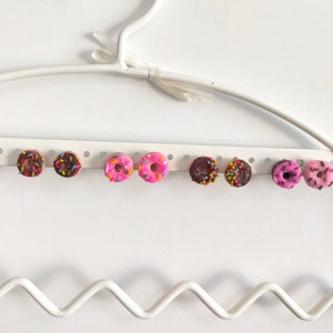 Puede incluir: Un conjunto de ocho pendientes en forma de donut con chispas de colores. Los pendientes son de color rosa, marrón y blanco.
