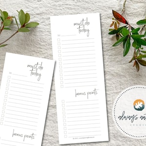 Op de afbeelding: Twee witte notitieblokken met de woorden "must do today" in zwart schrift. Elk notitieblok heeft een checklist-indeling met lijnen en vakjes. De woorden "bonus points" staan onderaan. Groene bladeren en een logo staan op de achtergrond.