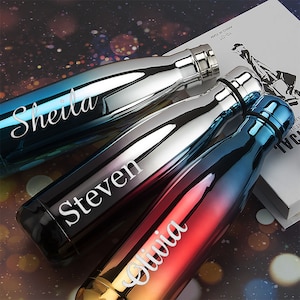 May include: Three stainless steel water bottles with a gradient colour design. The bottles are personalised with the names "Sheila", "Steven", and "Olivia".