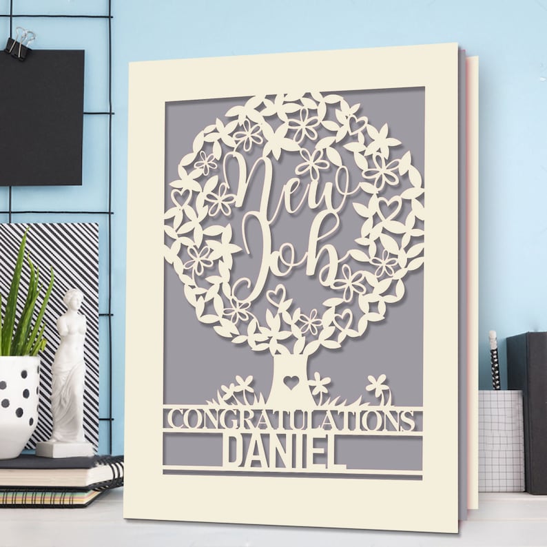 May include: A white card with a cut-out design of a tree with the words "New Job" inside the tree. The card has the words "Congratulations Daniel" at the bottom.