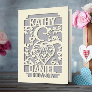 May include: A cream-colored card with a cut-out design featuring a heart, birds, and floral elements. The names "Kathy & Daniel" and the date "18/07/2019" are visible.
