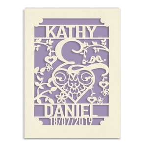 May include: A white paper cut-out design with a heart, floral vines, and two birds. The names "Kathy & Daniel" and the date "18/07/2019" are included in the design.