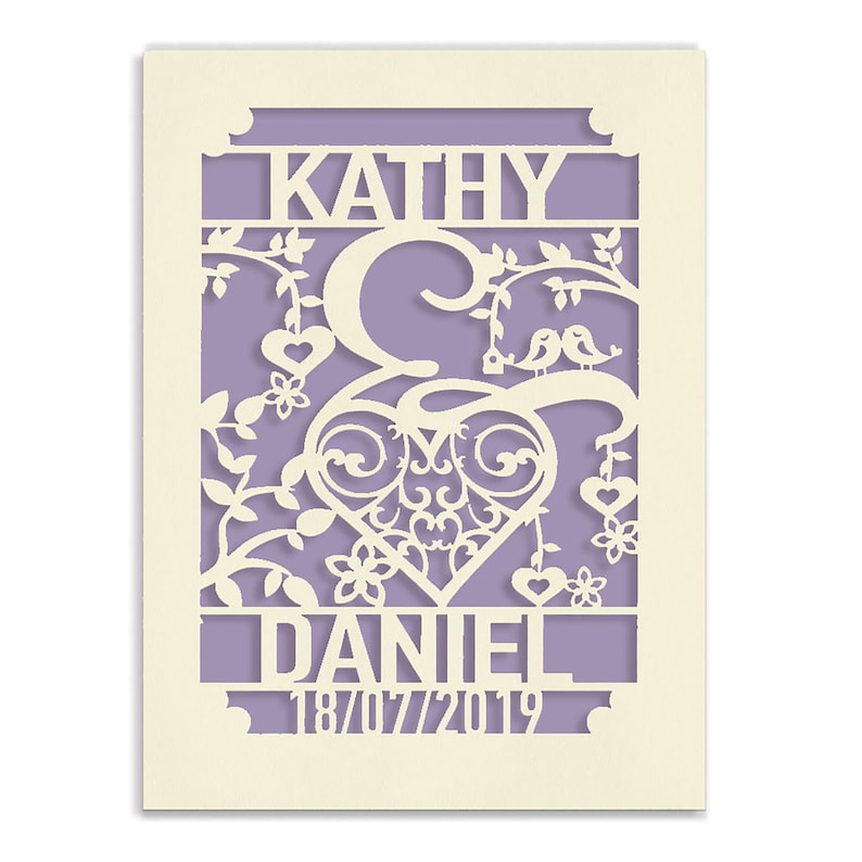 May include: A white paper cut-out design with a heart, floral vines, and two birds. The names "Kathy & Daniel" and the date "18/07/2019" are included in the design.
