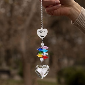Puede incluir: Un atrapasoles de cristal en forma de coraz&oacute;n con el nombre "Max" y una corona grabados en un dije en forma de coraz&oacute;n. Debajo, un arco&iacute;ris de cristales de colores conduce a un gran cristal facetado en forma de coraz&oacute;n. El atrapasoles cuelga de una cadena plateada.