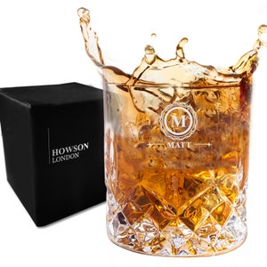 Puede incluir: Un vaso de whisky de vidrio transparente con un patr&oacute;n de diamante. El vaso est&aacute; lleno de l&iacute;quido &aacute;mbar y hielo. El vaso est&aacute; grabado con la letra "M" en un c&iacute;rculo y el nombre "Matt". El vaso est&aacute; sentado en una caja negra con las palabras "Howson London" impresas en &eacute;l.