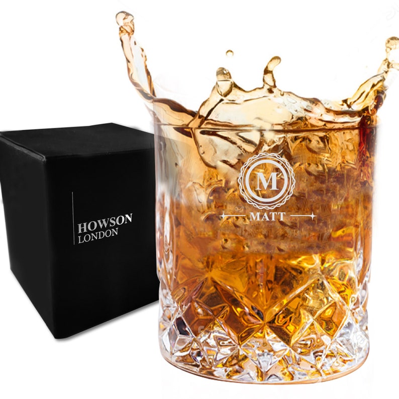 Puede incluir: Un vaso de whisky de vidrio transparente con un patr&oacute;n de diamante. El vaso est&aacute; lleno de l&iacute;quido &aacute;mbar y hielo. El vaso est&aacute; grabado con la letra "M" en un c&iacute;rculo y el nombre "Matt". El vaso est&aacute; sentado en una caja negra con las palabras "Howson London" impresas en &eacute;l.
