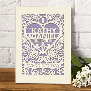 May include: A white card with a purple heart-shaped cutout featuring the names "Kathy & Daniel" and the date "19/06/2019". The heart is surrounded by a floral design and the words "Wedding Day" are printed below.