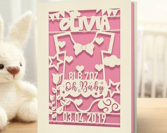 May include: A pink and white card with a cut-out design of a baby onesie, stars, flowers, and clouds. The card says "Olivia" and "Oh Baby" with the date "03.04.2019" and weight "8lb 7oz".