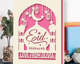 Può includere: Un biglietto bianco con un design a forma di moschea rosa tagliato con una luna crescente e stelle. Il testo "Eid Mubarak" è scritto in un carattere decorativo. Il biglietto include anche il testo "Love from Olivia".