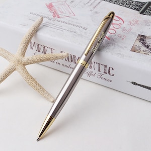 May include: A silver pen with a gold trim and a gold clip. The pen has the name "Tiana Swift" engraved on it.