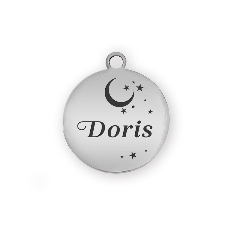 Puede incluir: Un charm redondo plateado con el nombre "Doris" en letra cursiva. El charm presenta un dise&ntilde;o de luna creciente y estrellas. Tiene un peque&ntilde;o lazo en la parte superior para sujetarlo.