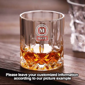 Puede incluir: Un vaso de rocas de vidrio transparente con un patr&oacute;n de diamante. El vaso est&aacute; lleno de l&iacute;quido &aacute;mbar. El vaso est&aacute; grabado con la letra "M" en un c&iacute;rculo y el nombre "MATT" debajo.