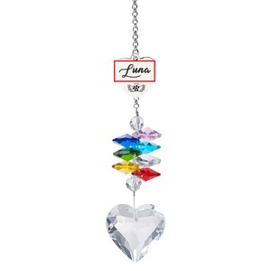 Puede incluir: Un atrapasoles de cristal con una cadena plateada. El atrapasoles presenta un cristal en forma de coraz&oacute;n en la parte inferior, una serie de cristales de colores y un dije en forma de coraz&oacute;n blanco con el nombre "Luna" en escritura negra.