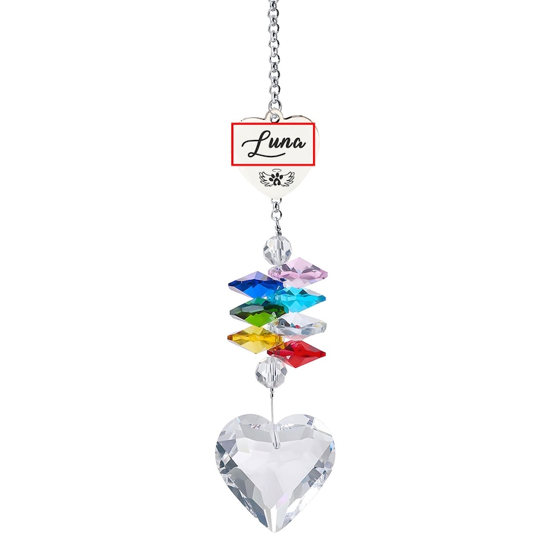 Puede incluir: Un atrapasoles de cristal con una cadena plateada. El atrapasoles presenta un cristal en forma de coraz&oacute;n en la parte inferior, una serie de cristales de colores y un dije en forma de coraz&oacute;n blanco con el nombre "Luna" en escritura negra.