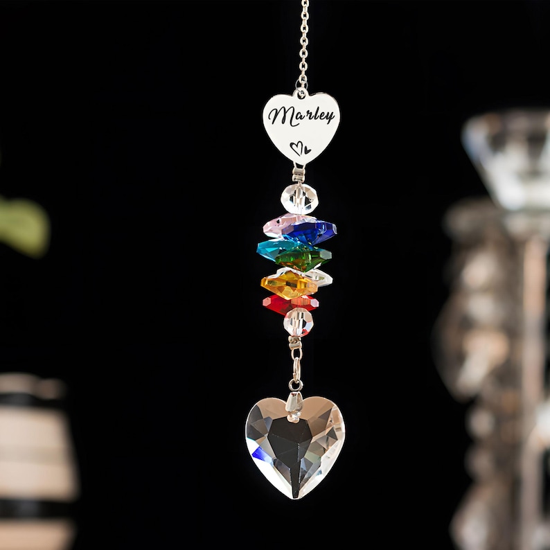 Puede incluir: Un atrapasoles de cristal en forma de coraz&oacute;n con el nombre "Marley" grabado en un coraz&oacute;n plateado. El atrapasoles presenta un arco&iacute;ris de cristales de colores y un gran cristal en forma de coraz&oacute;n en la parte inferior, suspendido por una cadena plateada.