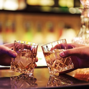 Puede incluir: Dos vasos de cristal llenos de l&iacute;quido &aacute;mbar y cubitos de hielo. Los vasos se levantan para brindar.