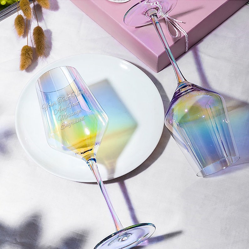 May include: Two iridescent wine glasses with a rainbow effect. The glass on the left has the text "Your Text Here Any Text Message Engraved" etched on the side.