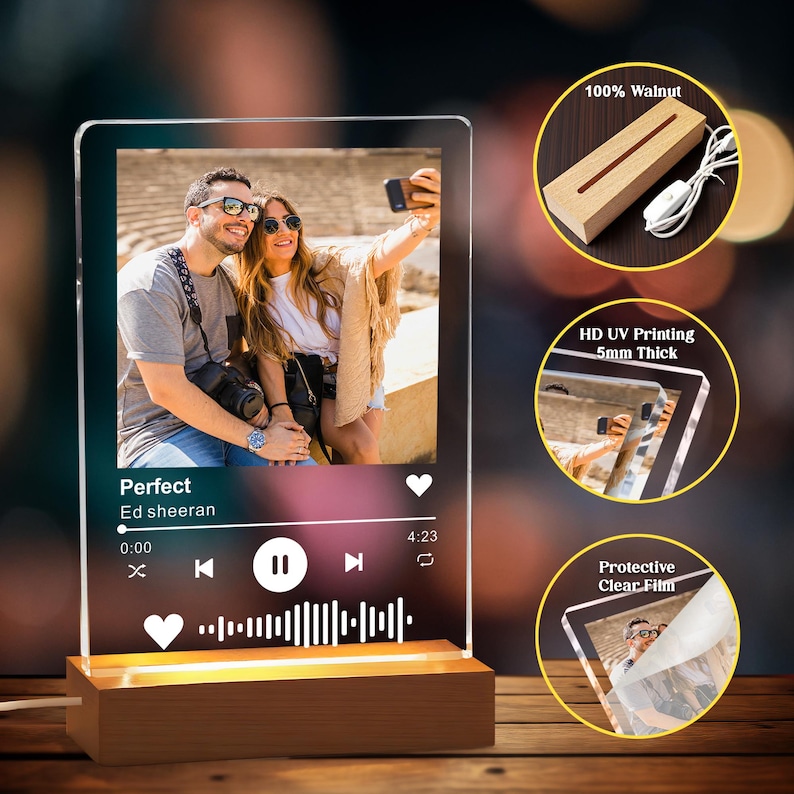 May include: A clear acrylic photo display with a wooden base, featuring a couple taking a selfie. The display includes a music player interface with the song title "Perfect" by Ed Sheeran. The base is made of walnut and has a warm light.