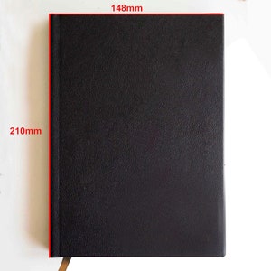 May include: A black notebook with a textured cover and a vertical spine. Red text on the image indicates dimensions of 148mm by 210mm. A small portion of a tan ribbon bookmark is visible extending from the bottom edge of the rectangular notebook.
