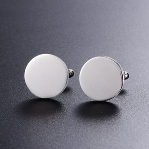 May include: A pair of silver cufflinks with a round, smooth, blank surface.