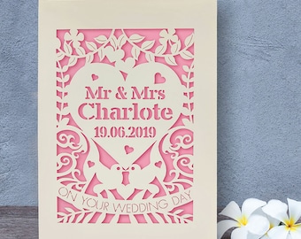 May include: A white card with a pink cutout design featuring a heart with the text "Mr & Mrs Charlotte 19.06.2019" and the words "On Your Wedding Day" below.