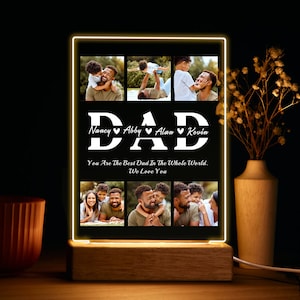 May include: A black illuminated photo frame with a wooden base. The frame displays a collage of photos of a man with his children. The text "DAD" is displayed in white with hearts and the names "Nancy", "Abby", "Alan", and "Kevin" below. The text "You Are The Best Dad In The Whole World. We Love You" is displayed below the collage.