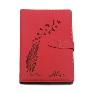 Puede incluir: Diario de cuero rojo con un dise&ntilde;o grabado con l&aacute;ser de una pluma y p&aacute;jaros en vuelo. El diario tiene un cierre de solapa y el nombre "Alice" est&aacute; inscrito en la portada. Un accesorio elegante para escribir y tomar notas.