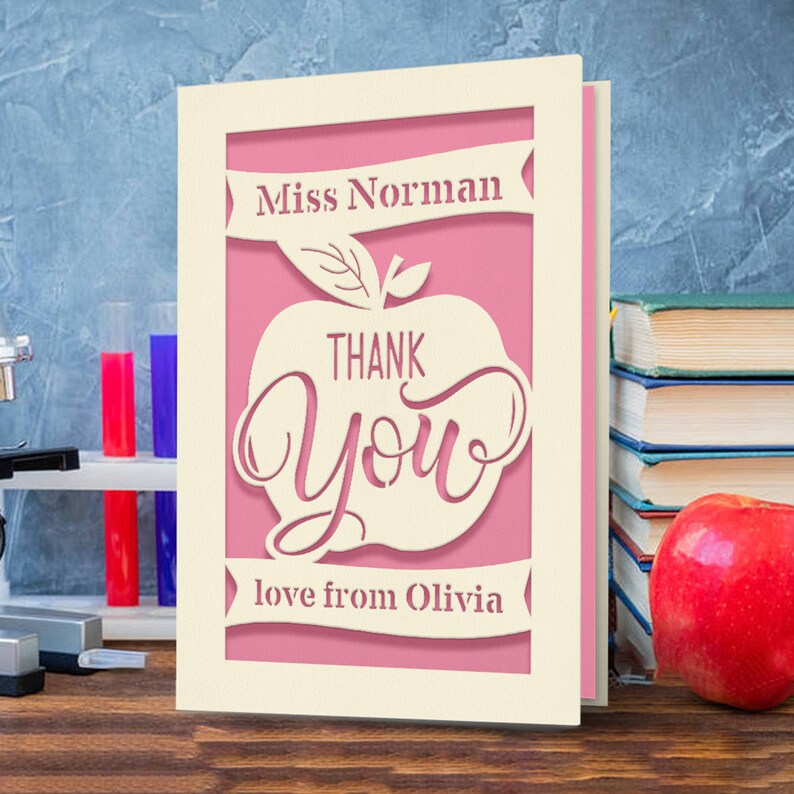 May include: A pink and white card with a cut-out apple design. The apple says "Thank You" and has a green leaf. The card has the text "Miss Norman" and "love from Olivia" on it.