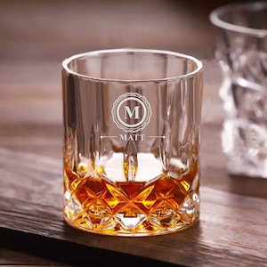 Puede incluir: Un vaso de rocas de vidrio transparente con un patr&oacute;n de diamante. El vaso est&aacute; lleno de l&iacute;quido &aacute;mbar y tiene la letra "M" y el nombre "MATT" grabados en la parte delantera.