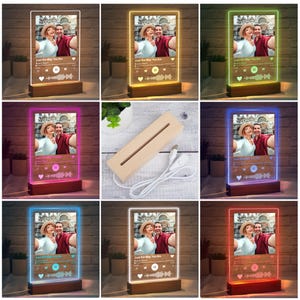 May include: A personalized LED night light featuring a photo and music player interface design. The acrylic panel displays a couple's photo and song details, with a wooden base. The light has a rectangular shape and is illuminated with various colors.