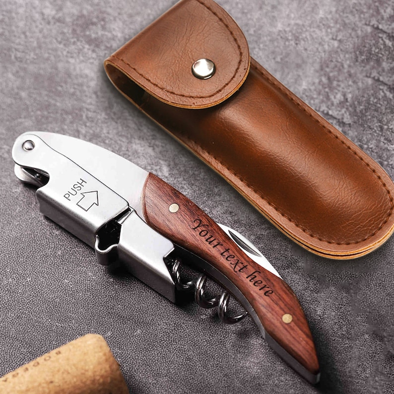 May include: A silver and wood wine opener with a brown leather carrying case. The opener has a corkscrew, a foil cutter, and a bottle opener. The wood handle is engraved with the text "Your text here".