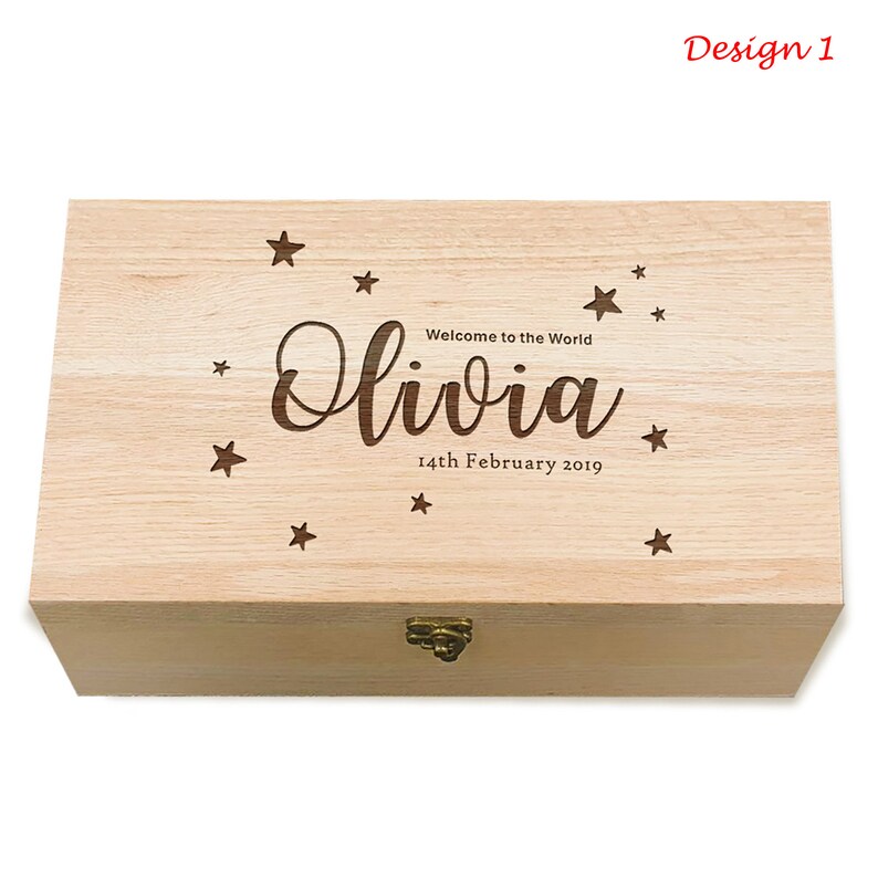 May include: A light wood keepsake box with a hinged lid and a brass latch. The top of the box is engraved with the text "Welcome to the World Olivia 14th February 2019" and a scattering of stars.