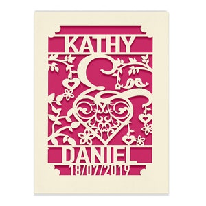 May include: A white paper cut-out design with a pink background. The design features a heart with a decorative flourish, two birds, and the names "Kathy & Daniel" with the date "18/07/2019".