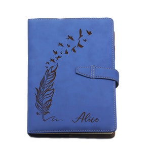 Puede incluir: Un diario de cuero azul con un dise&ntilde;o de pluma y p&aacute;jaros. El diario tiene un cierre de solapa y el nombre "Alice" est&aacute; impreso en la portada. El diario mide aproximadamente 20 cm de alto y 15 cm de ancho.