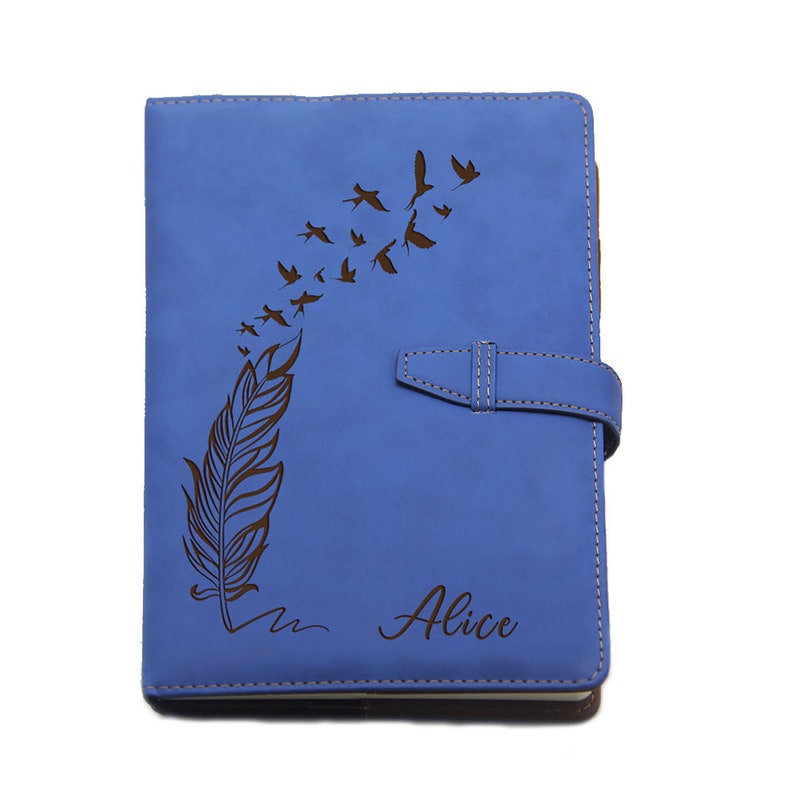 Puede incluir: Un diario de cuero azul con un dise&ntilde;o de pluma y p&aacute;jaros. El diario tiene un cierre de solapa y el nombre "Alice" est&aacute; impreso en la portada. El diario mide aproximadamente 20 cm de alto y 15 cm de ancho.