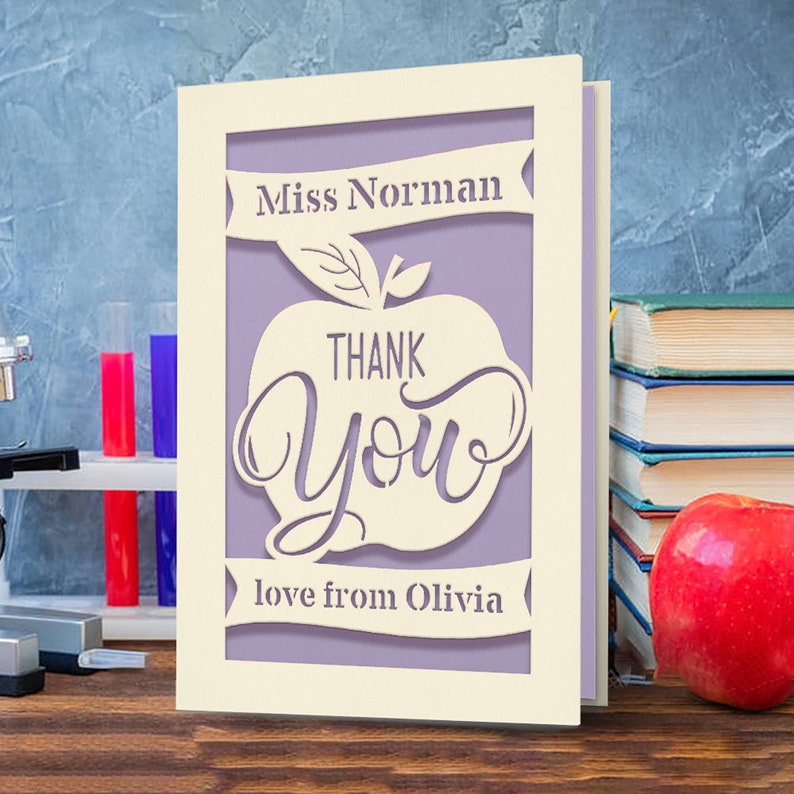 May include: A white card with a purple apple design. The apple has the words "Thank You" inside. The card says "Miss Norman" and "love from Olivia".