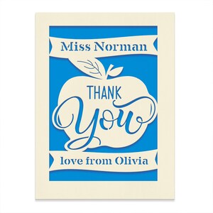 May include: A white card with a blue background and a white apple with the words "Thank You" inside. The card also has the text "Miss Norman" and "love from Olivia" on it.