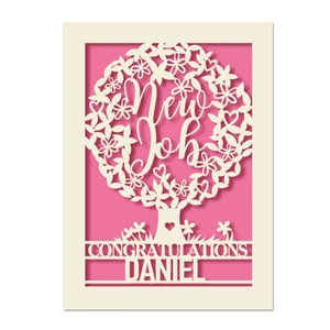 May include: A white card with a pink background and a cut-out design of a tree with the words "New Job" inside the tree. The card also has the words "Congratulations Daniel" at the bottom.