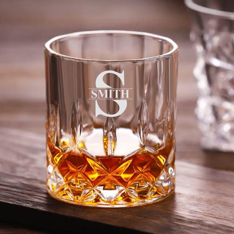 May include: A clear glass whiskey tumbler with a diamond-shaped pattern. The glass is filled with amber liquid and has the letter "S" and the word "SMITH" etched on the front.