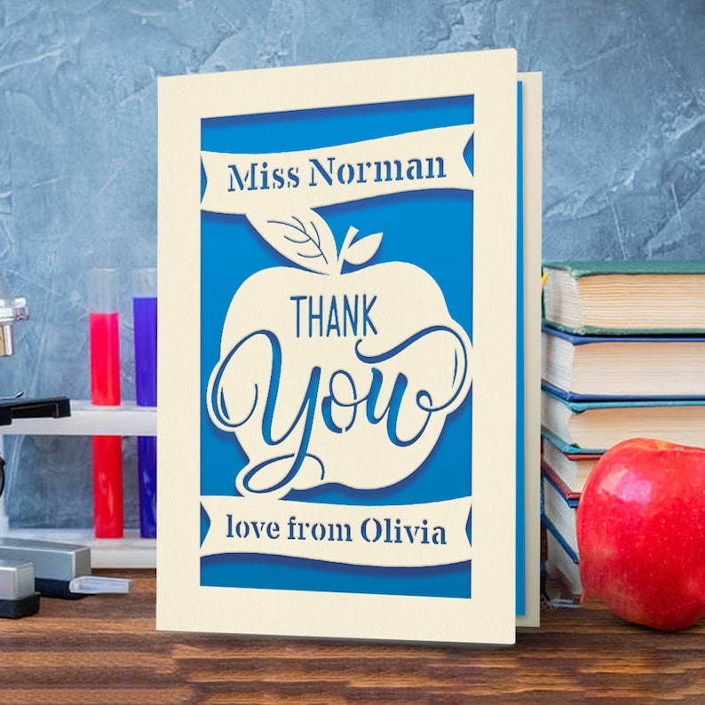 May include: A white card with a blue apple design. The apple has the words "Thank You" inside. The card says "Miss Norman" at the top and "love from Olivia" at the bottom.