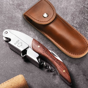 May include: A silver and wood wine opener with a brown leather carrying case. The opener has a wooden handle with the text "Your text here" engraved on it. The opener also has a push button and a corkscrew.