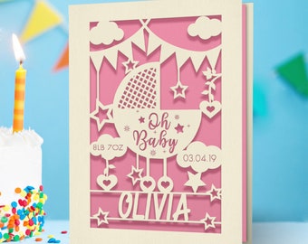 May include: A pink and white laser cut card with a baby carriage design. The card says "Oh Baby" and includes the name "Olivia", the date "03.04.19", and the weight "8LB 7OZ".