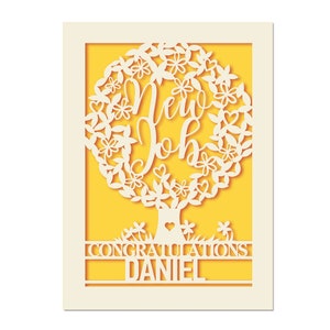 May include: A white paper card with a yellow background. The card features a cut-out design of a tree with the words "New Job" in the center. The text "Congratulations Daniel" is at the bottom of the card.